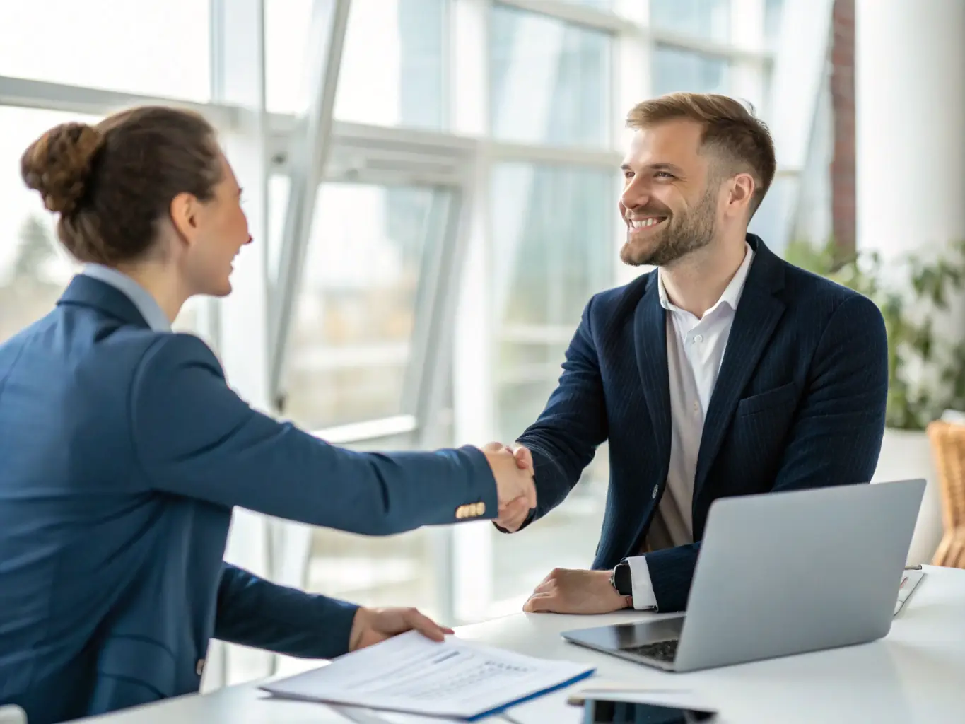 A photograph of a person in a business suit confidently shaking hands with an interviewer in a bright, modern office, symbolizing job training and employment opportunities.